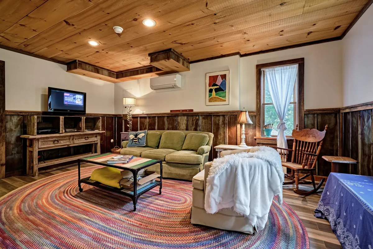 A vibrant interior scene showcasing a green sofa, a colorful rug, a wooden rocking chair, a TV, and playful artwork on the wall. The arrangement of comfortable seating and fun accents create an atmosphere designed for relaxation and socializing.