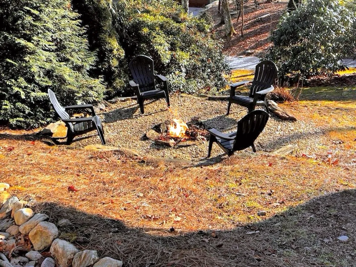 The image centers on a cozy fire pit area with black chairs nestled amidst vibrant greenery. The seating arrangement invites guests to gather, share stories, and enjoy the warmth of the fire surrounded by the tranquility of nature. The overall feeling is one of intimate seclusion, ideal for stargazing or evening relaxation.