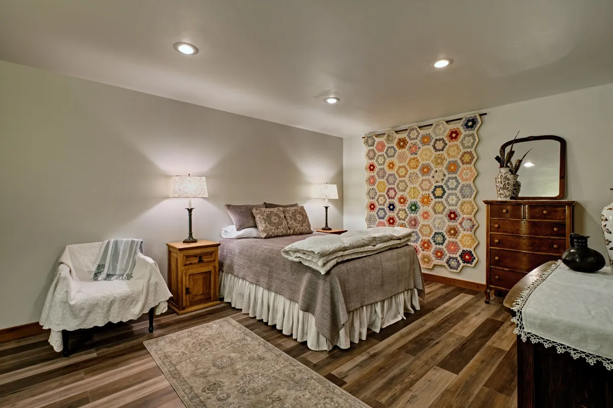 This scene highlights a plush bed with a decorative quilt, a colorful wall hanging, and a wooden dresser, evoking a warm, inviting mood ideal for reading or quiet relaxation.